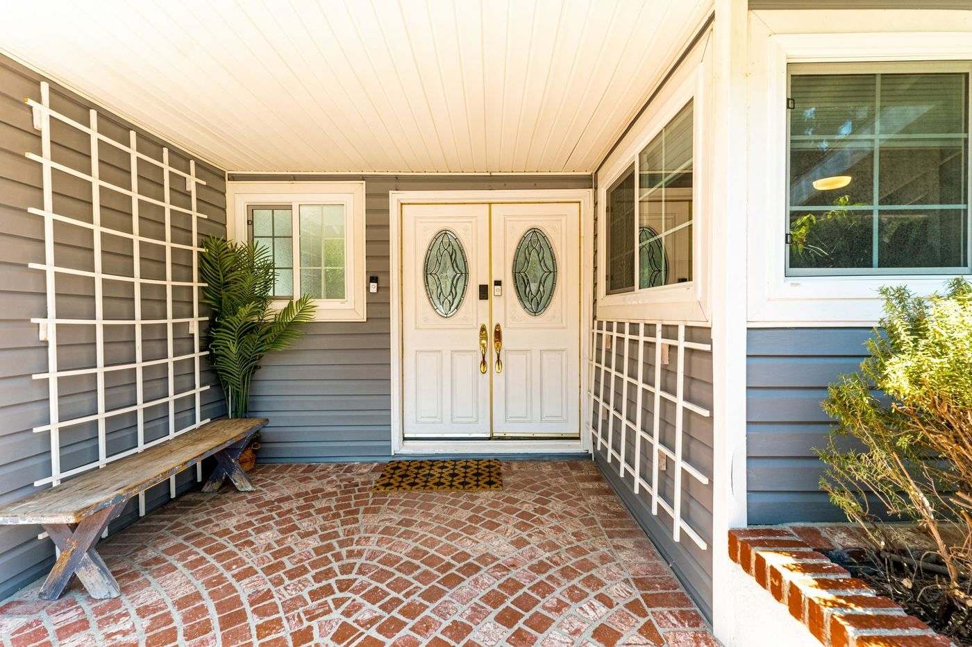 White double front doors on a brick house, with a walkway and a bench
