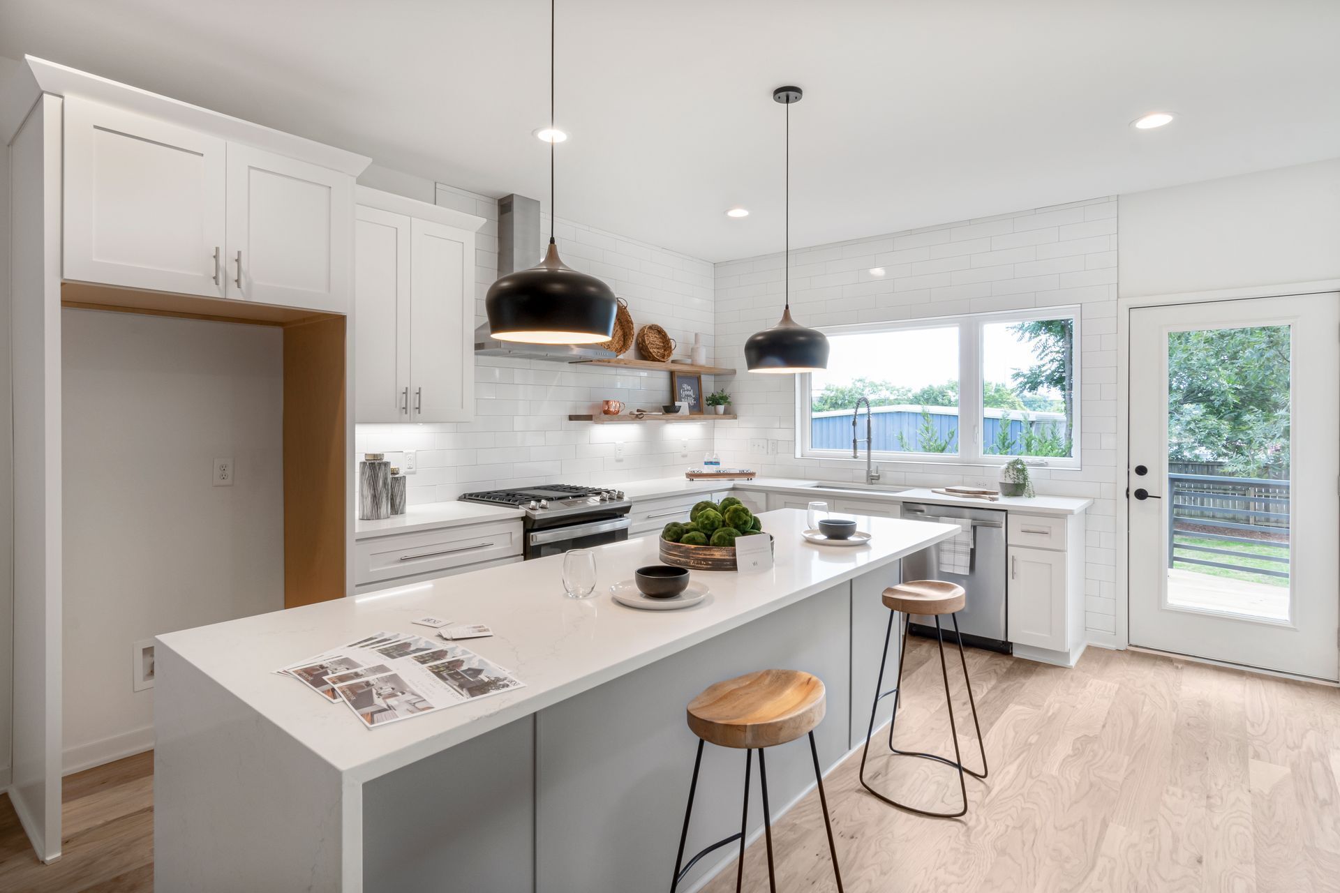 A bright white kitchen with an island and wooden stools