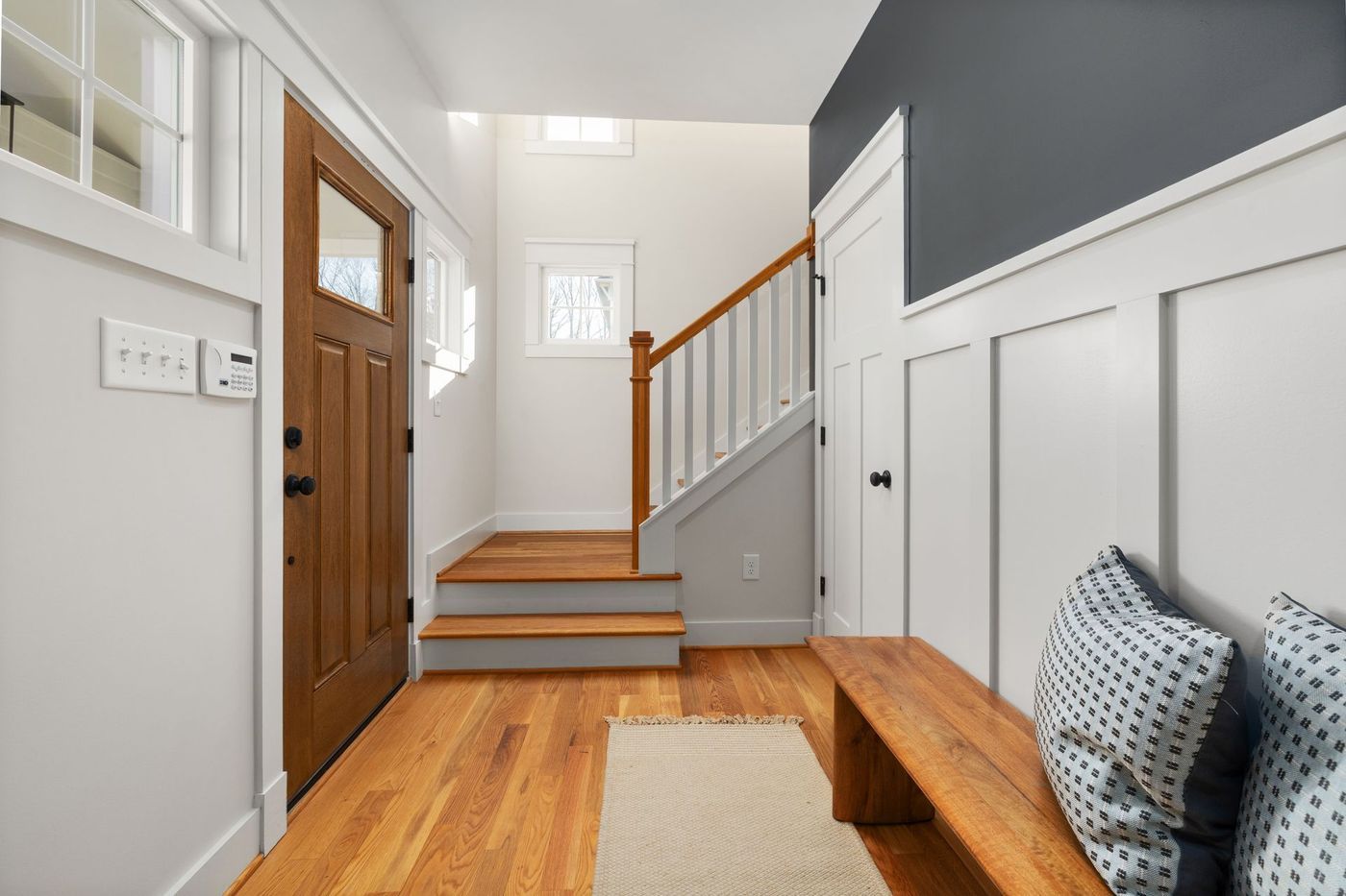 A bright entryway with a wooden front door, stairs and a bench